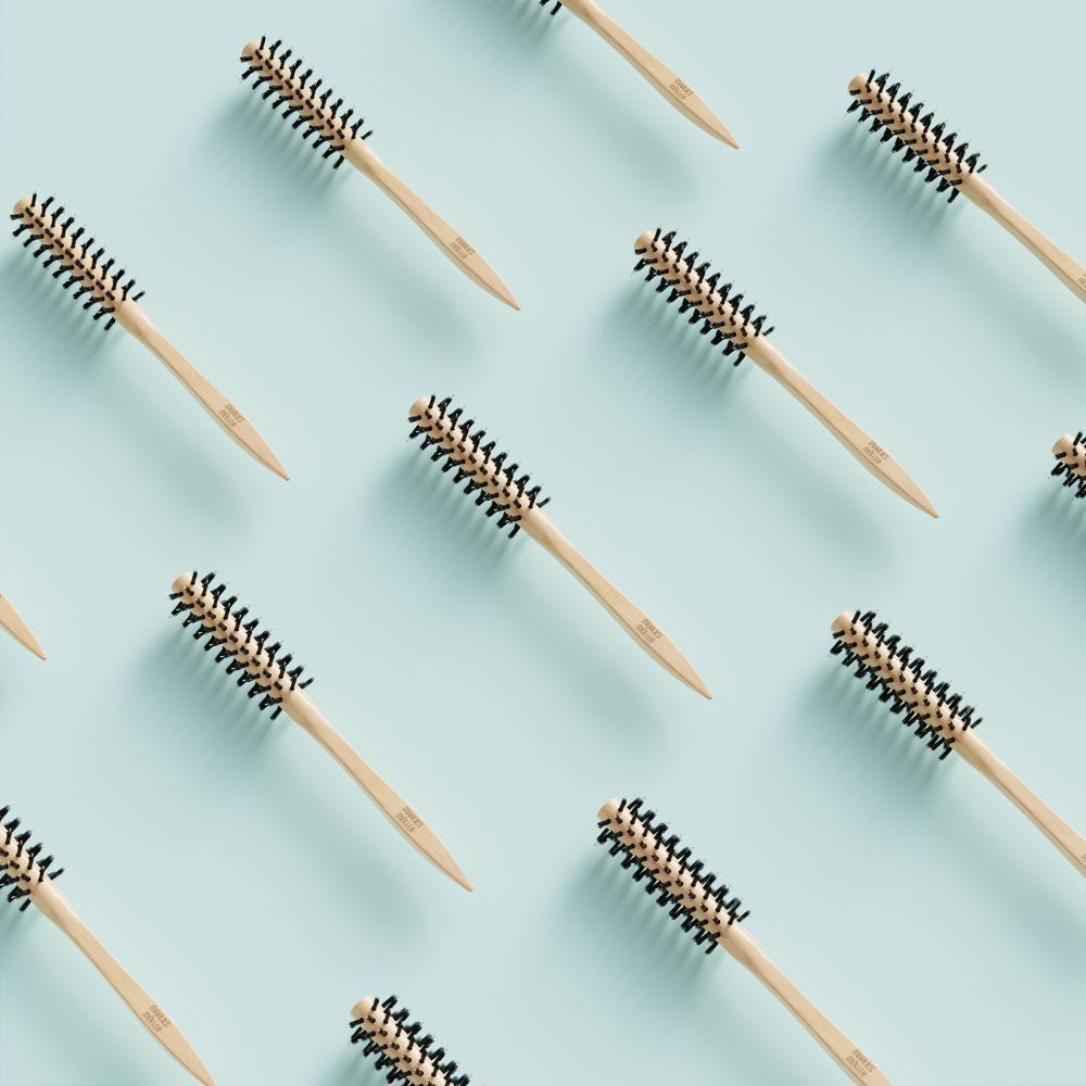 Motif de brosses à cheveux rondes sur fond bleu clair. Manche en bois, poils noirs. Pas de marque visible.