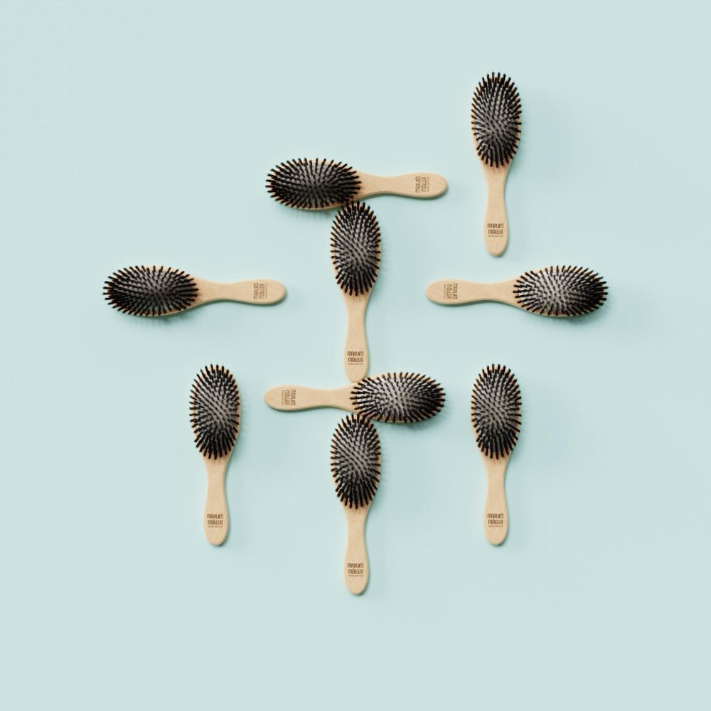 Mehrere kleine ovale Haarbürsten auf türkisfarbenem Hintergrund. Holzgriff, schwarze Borsten.