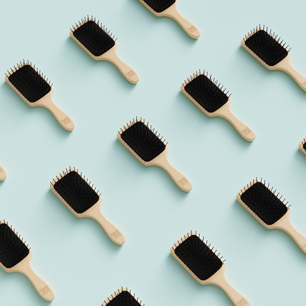 Plusieurs brosses à cheveux avec manche en bois et coussin noir. Sur fond bleu clair.