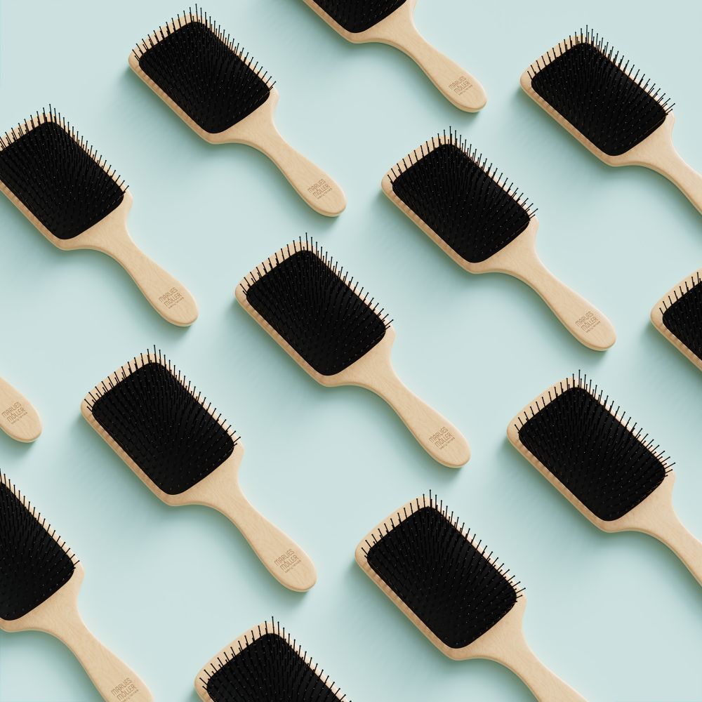 Plusieurs brosses à cheveux avec manche en bois et coussinet noir, sur fond bleu clair.