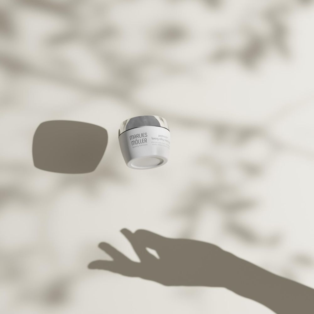 Weißer Tiegel mit silbernem Deckel, schwebend. Produktname: Marlies Möller Pashmisilk Luxury Silky Cream Mask.