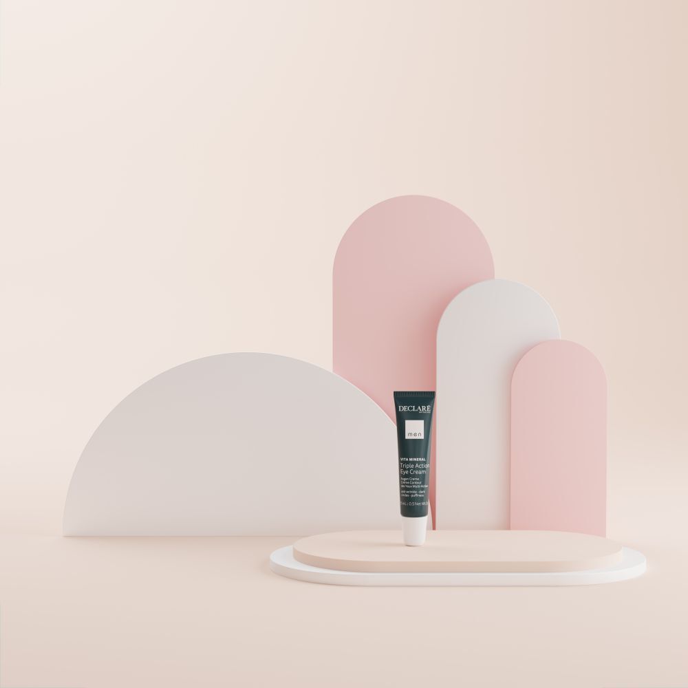 Blaue Tube DECLARÉ Augencreme auf Podest. Hintergrund mit Formen in Rosa und Weiß.