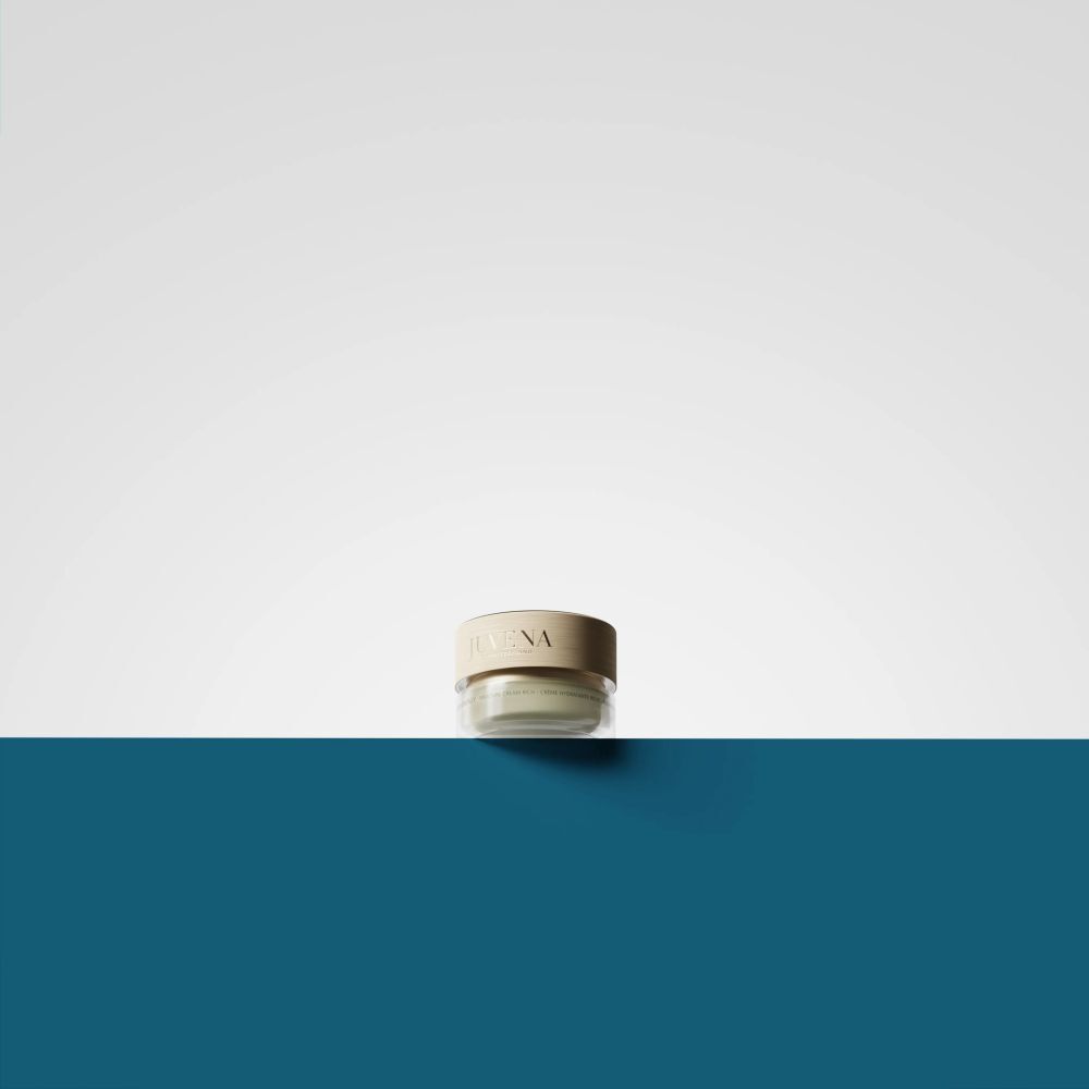 Petit pot de crème avec couvercle doré. Inscription : Juvena. Sur fond bleu et blanc.