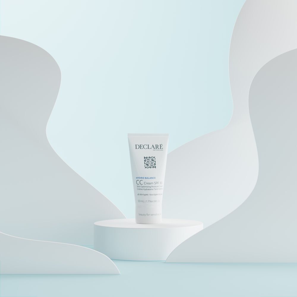 Weiße Tube DECLARÉ CC Cream SPF 30 auf einem Podest. Hintergrund mit weißen, geschwungenen Formen.