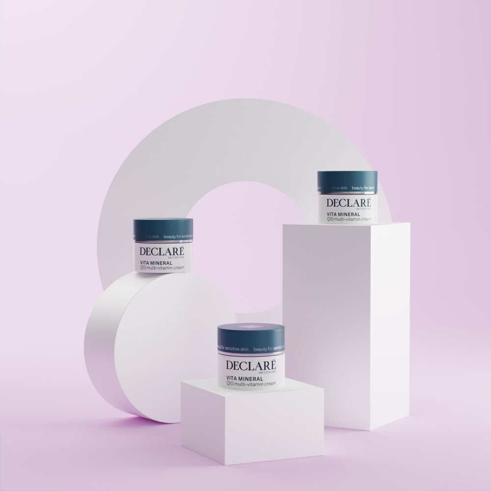 Trois pots de crème sur socles. DECLARÉ Vita Mineral Q10 Multi-Vitamin Crème. Fond rose.