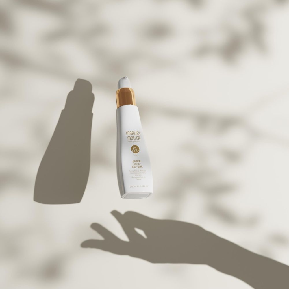 Weiße Flasche mit goldenem Verschluss. Aufschrift: Marlies Möller, Luxury Golden Caviar Hair Bath. Schatten einer Hand.