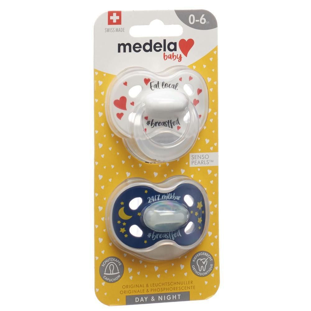 Zwei Schnuller in Verpackung. Der obere hat rote Herzen und Text. Der untere hat Sterne und Mond. Marke: Medela Baby.
