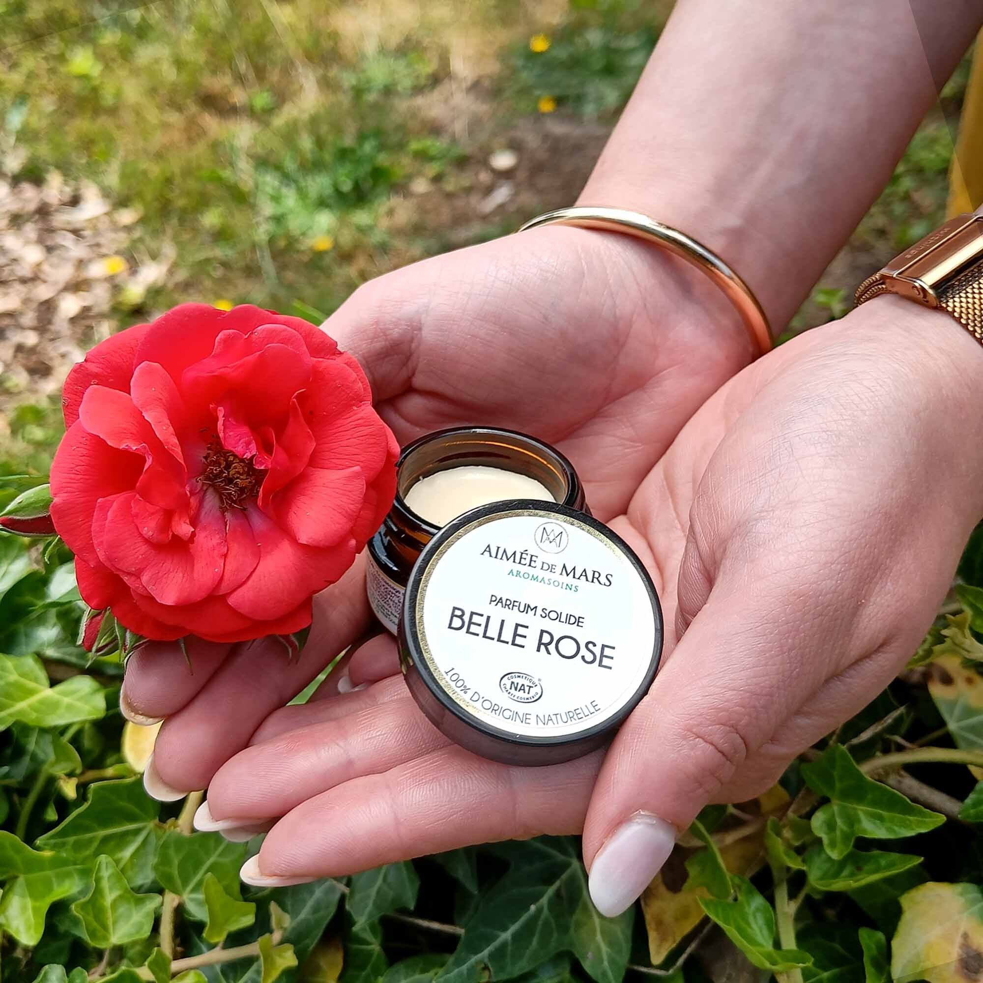 Mains tenant un pot ouvert avec "Belle Rose" et une rose rouge. Sur le pot, "Parfum Solide".