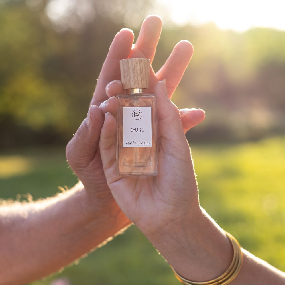 Flacon de parfum dans les mains. Bouchon en bois, étiquette avec logo, "EAU 21" et "Aimée de Mars".