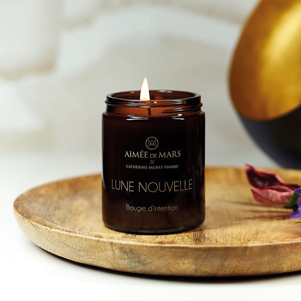 Braune Kerze in einem Glasbehälter mit schwarzem Deckel. Kerze brennt. Aufschrift: Aimée de Mars, Lune Nouvelle, Bougie d'intention.