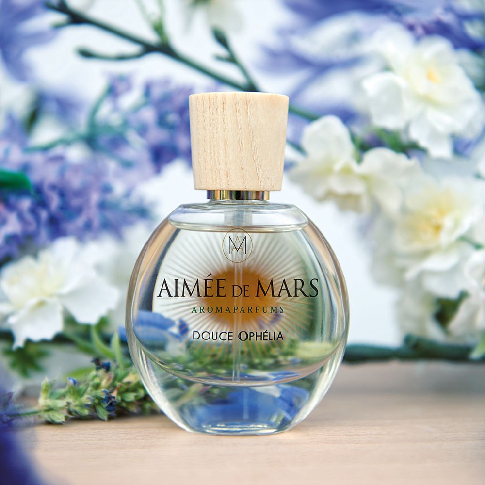 Glasflakon mit Holzverschluss. Aufschrift: Aimée de Mars, Douce Ophélia. Hintergrund: Blumen und Holz.