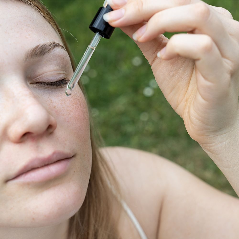 Frau mit geschlossenen Augen. Tropfer gibt Flüssigkeit auf die Haut. Grüner Hintergrund.