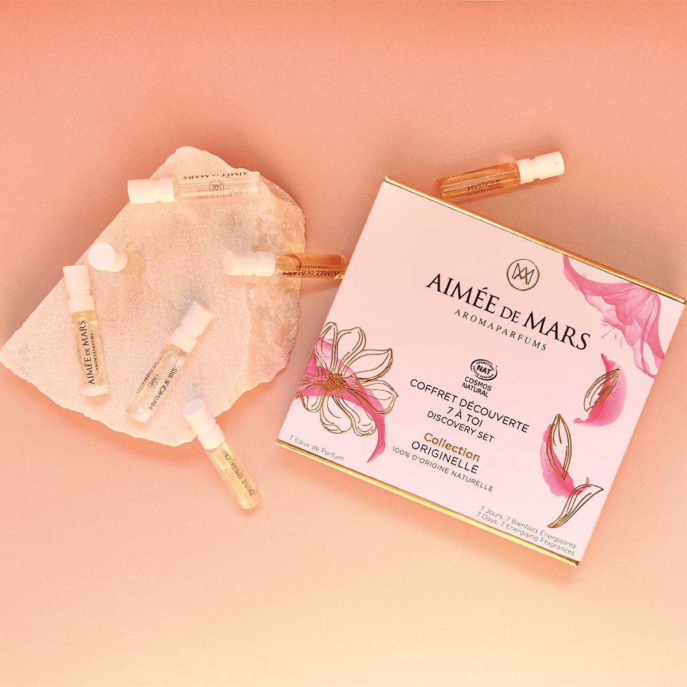 Aimée de Mars® Discovery Set Collection. Eine Schachtel und sieben kleine Flakons auf rosa Untergrund. Blütenblätter.