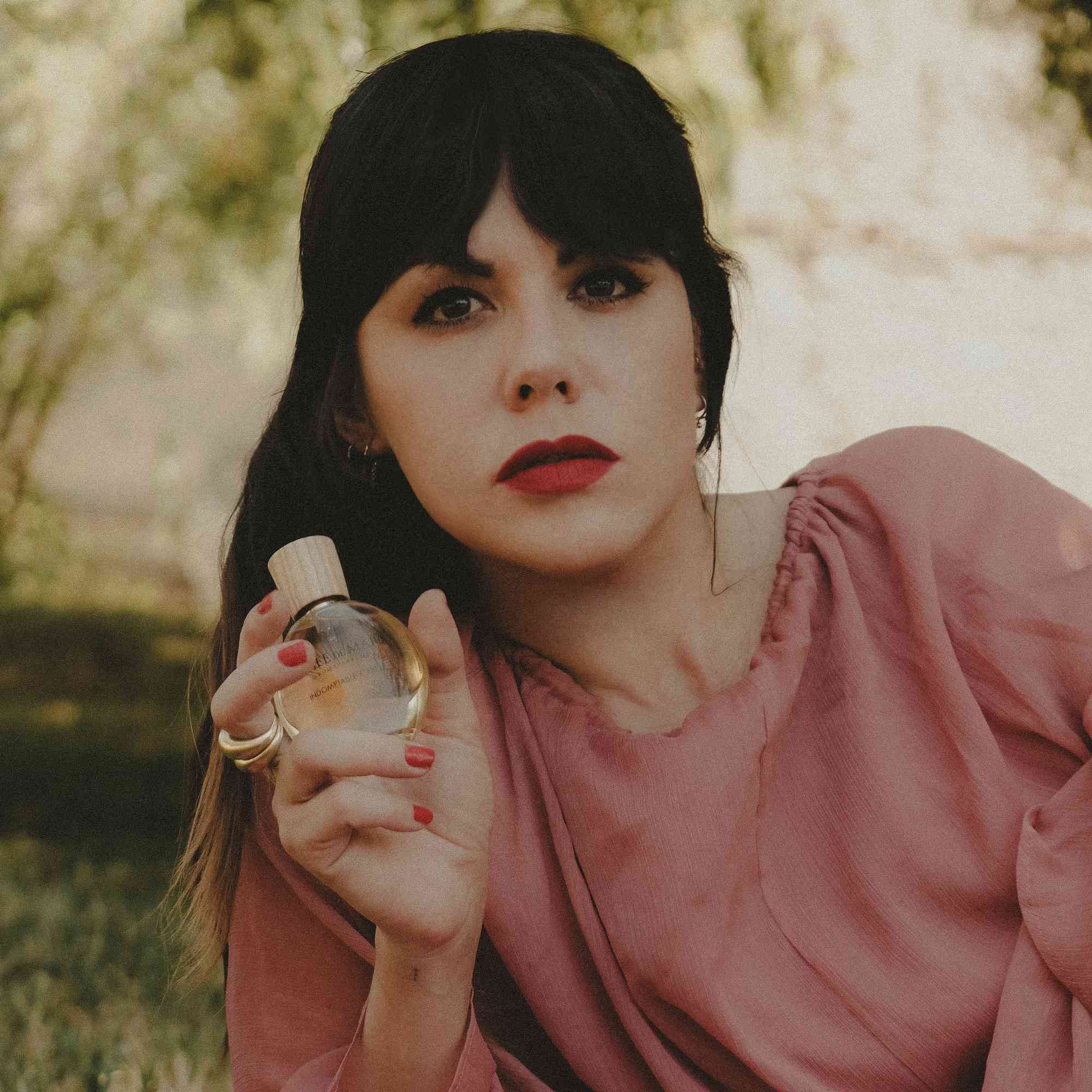 Frau hält einen Flakon. Sie trägt rotes Lippenstift und einen Ring. Der Flakon ist sichtbar.