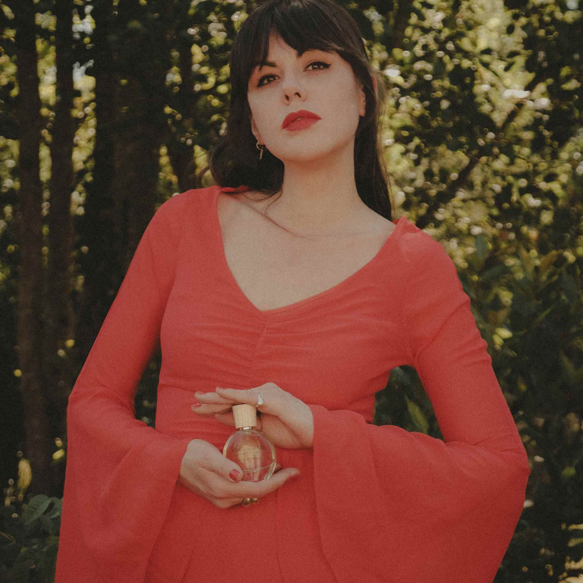 Frau hält einen Flakon. Sie trägt ein rotes Kleid. Der Flakon ist sichtbar.