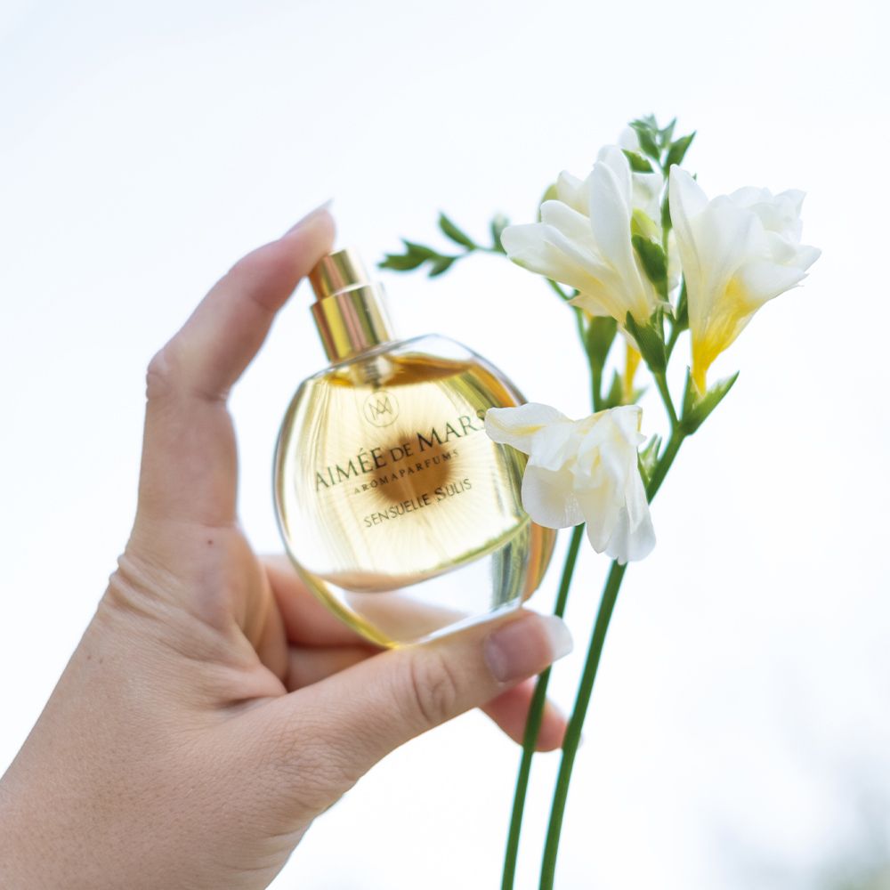 Hand hält einen runden Glasflakon mit goldener Flüssigkeit. Aufschrift: Aimée de Mars Aromaparfums, Sensuelle Sulis.