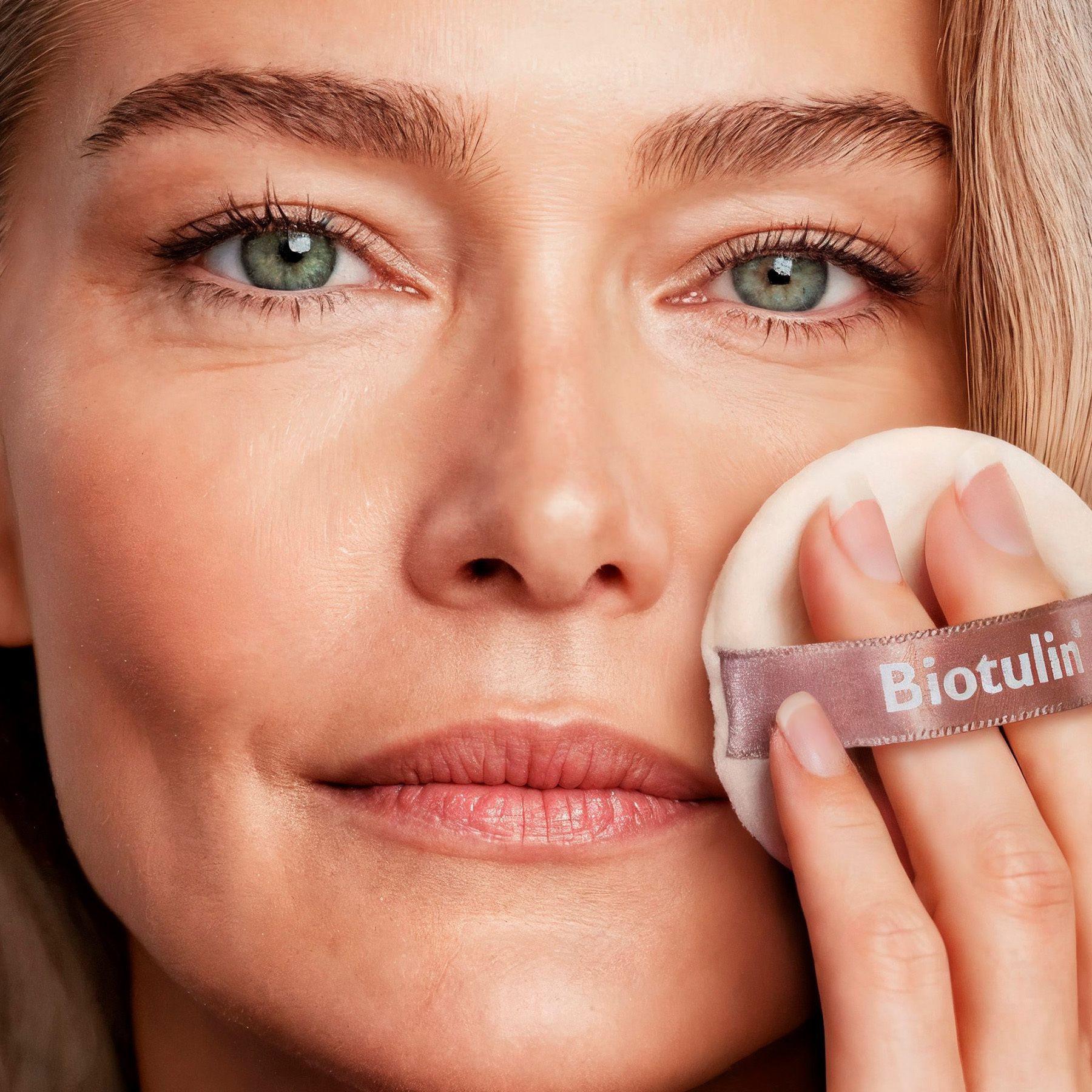 Frau mit Puderquaste. Auf der Quaste steht Biotulin. Der Hintergrund ist hell.