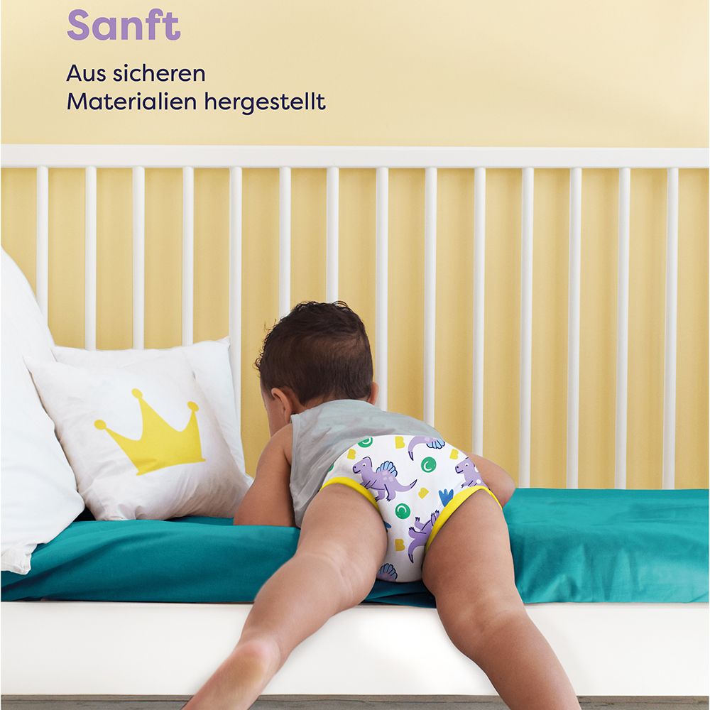 Kind mit Lernhöschen liegt auf Bett. Text: Sanft. Aus sicheren Materialien hergestellt. Marke: Bambino Mio.
