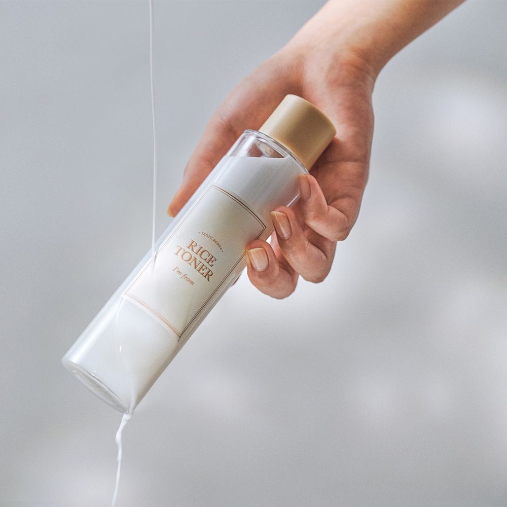 Hand hält eine durchsichtige Flasche mit weißer Flüssigkeit und der Aufschrift 'RICE TONER'.