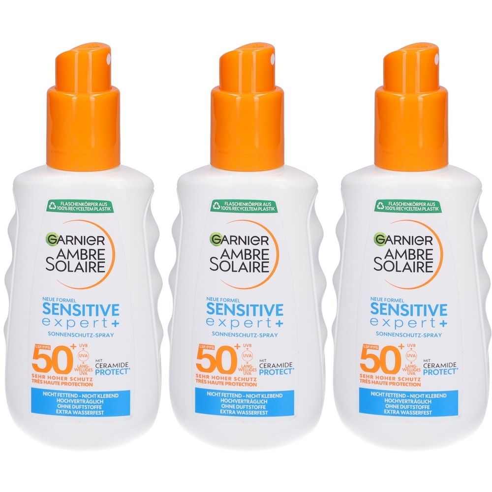 Drei Flaschen Sonnenspray mit orangefarbenem Sprühkopf. Aufschrift: GARNIER AMBRE SOLAIRE Sensitive Expert+ 50.