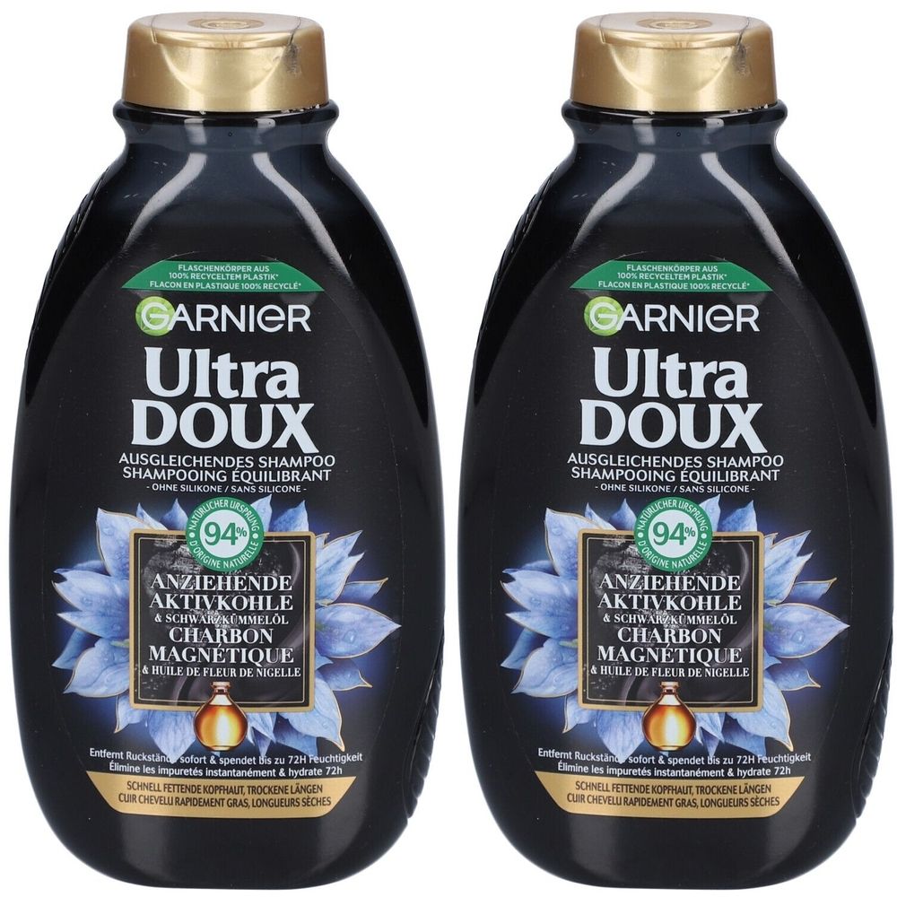 Deux flacons de shampooing noirs. Inscription: GARNIER Ultra DOUX. Contient du charbon actif et de l'huile de nigelle. Fleur bleue et bouchon doré.