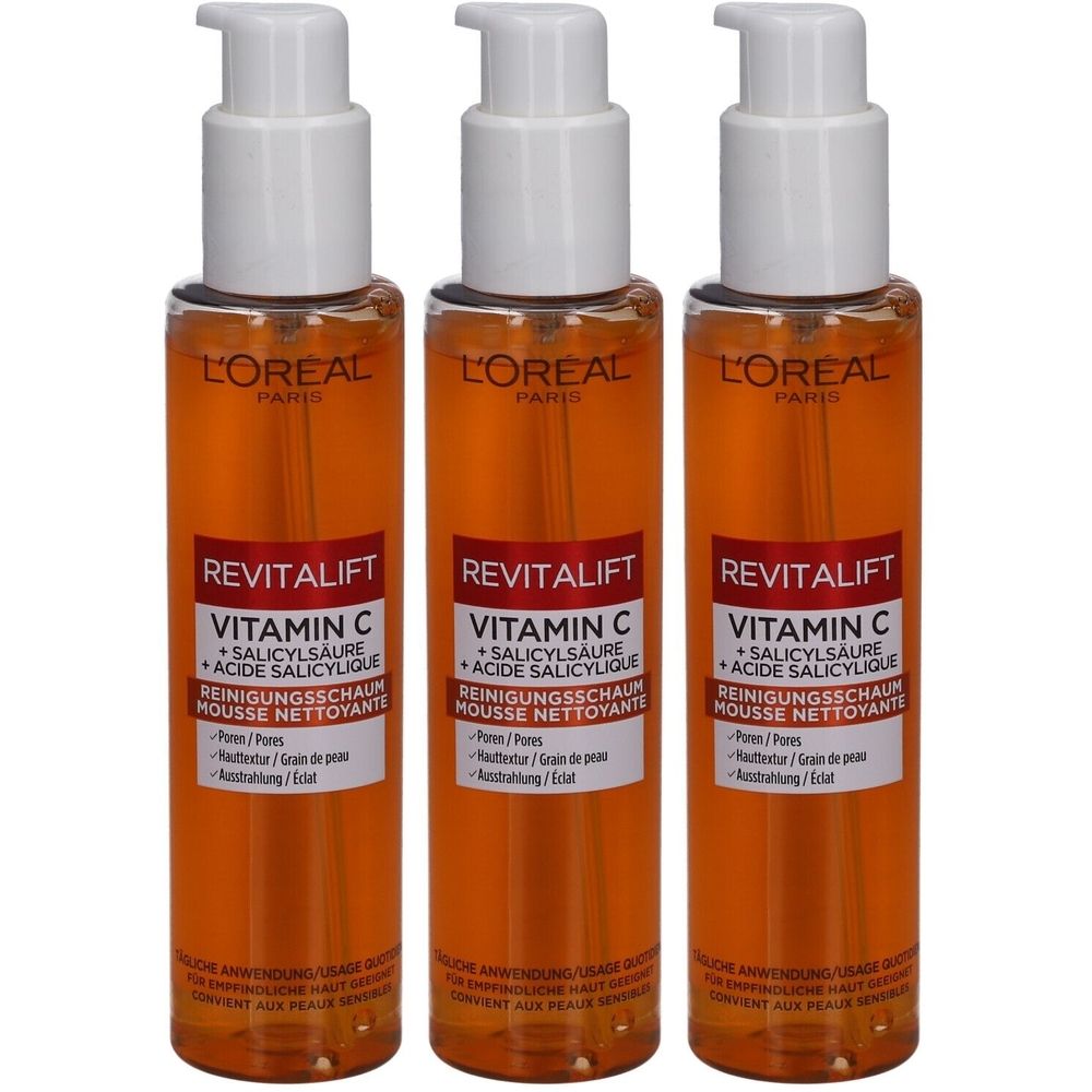 Trois flacons de mousse nettoyante Revitalift L'Oréal avec vitamine C et acide salicylique. Pompes blanches, liquide orange, étiquettes de produit.