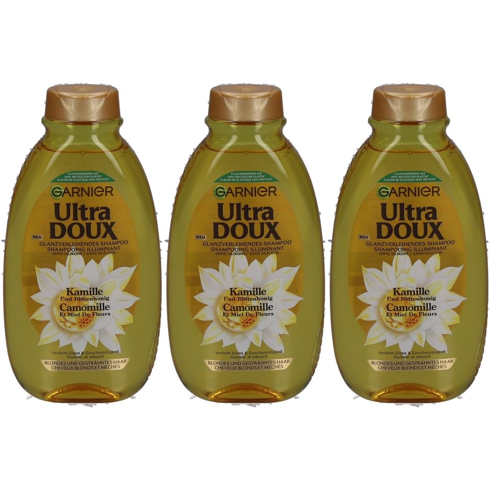 Drei Flaschen Garnier Ultra Doux Shampoo Illuminating Camomile. Grünliche Flaschen mit goldenen Deckeln und Etiketten mit Kamillenblüten.