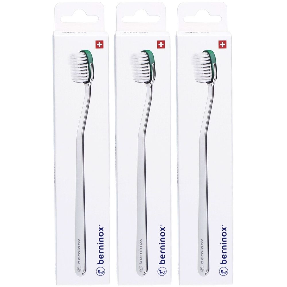 Trois brosses à dents dans leur emballage. Les brosses ont un manche courbé et une tête verte. Un symbole de croix suisse est visible sur l'emballage.