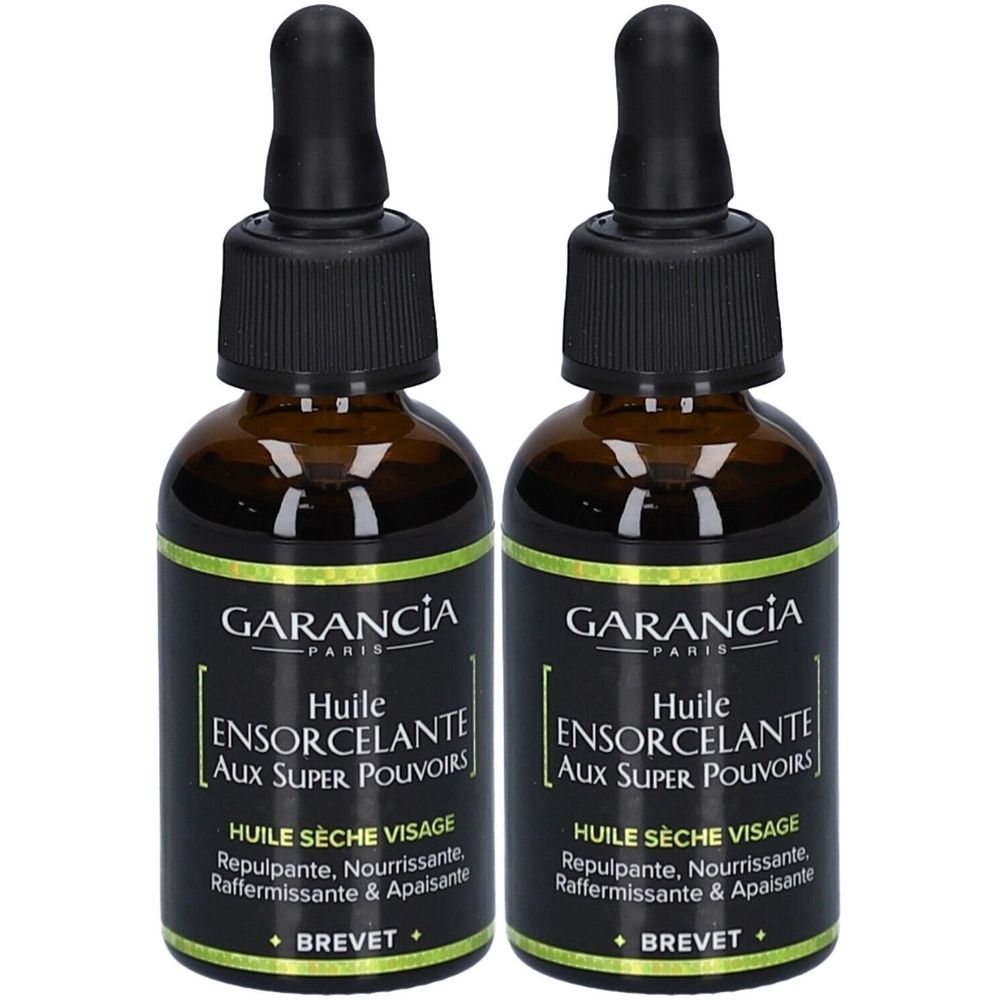 Zwei Flaschen Gesichtsöl. Braune Glasflaschen mit schwarzem Deckel und Pipette. Schwarzes Etikett mit weißer Schrift: GARANCIA, Huile Ensorcelante.