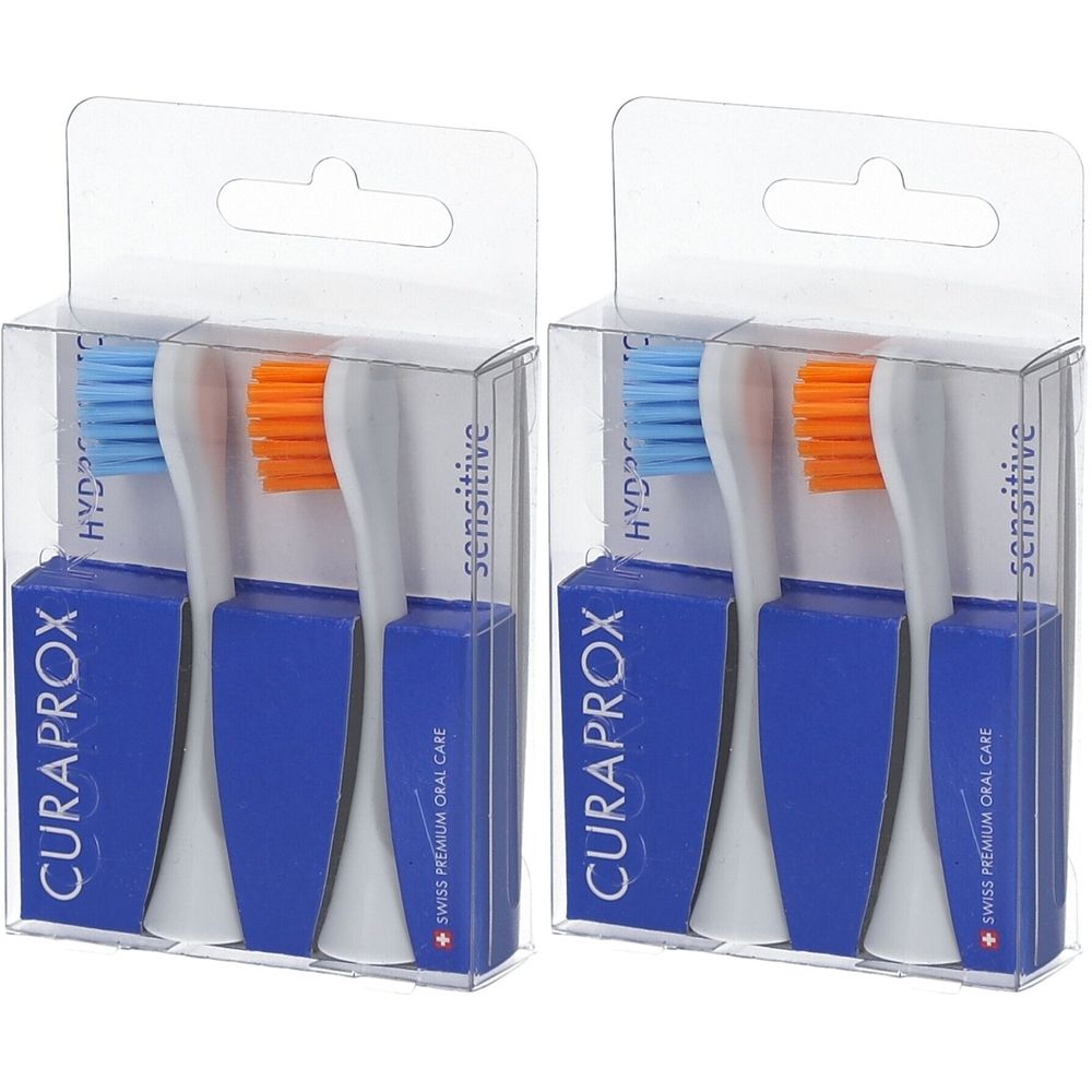 Zwei Zahnbürstenköpfe in transparenten Kunststoffverpackungen. Blaue und orangefarbene Borsten. Blaue Basis mit CURAPROX-Logo.