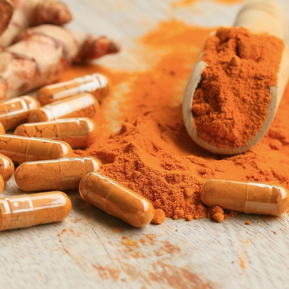 Kapseln, Kurkuma-Pulver und Kurkuma-Wurzeln auf Holz. Kapseln orangefarben. Pulver und Wurzeln braun.