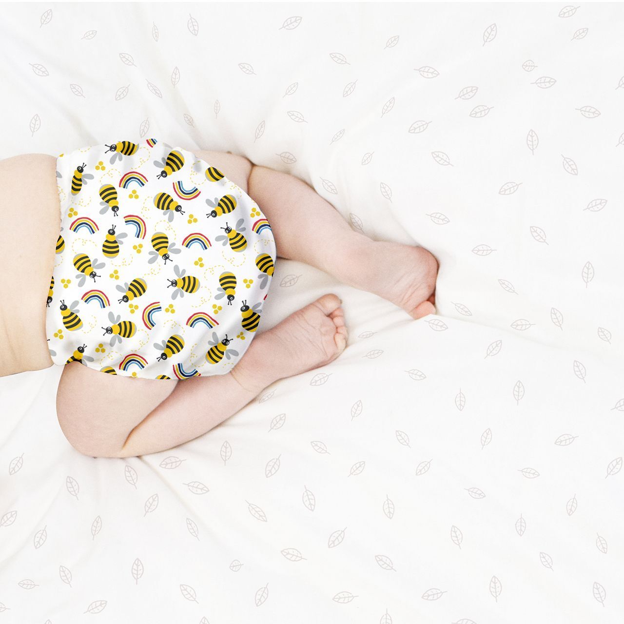 Bébé couché sur le ventre, portant une couche lavable avec motif abeilles et arcs-en-ciel.