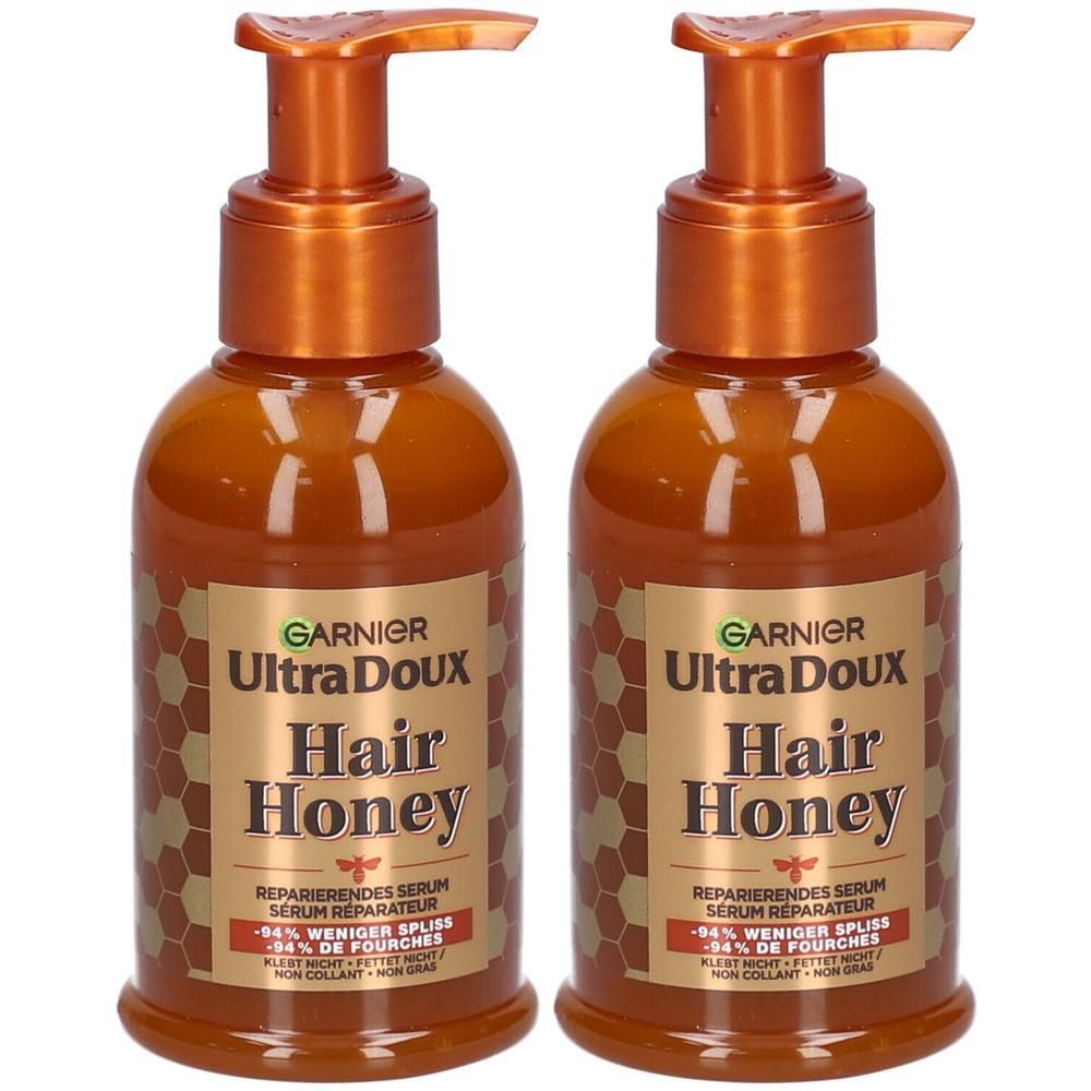 Deux flacons de sérum Garnier Ultra Doux Hair Honey avec distributeurs à pompe. Étiquettes dorées à motif nid d'abeille.