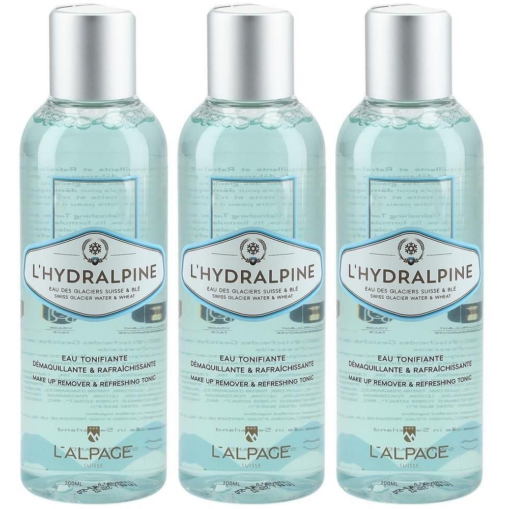 Trois flacons de tonique facial L'Hydralpine. Liquide clair dans des bouteilles cylindriques avec des bouchons argentés. Étiquettes avec texte.