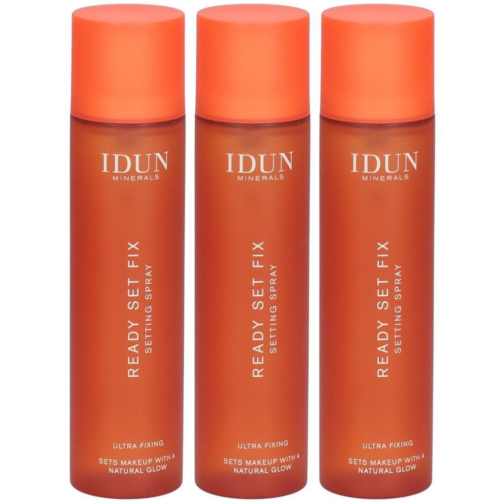 Drei orangefarbene Sprühflaschen mit orangefarbenen Deckeln. Auf jeder Flasche steht "IDUN Minerals Ready Set Fix Setting Spray".