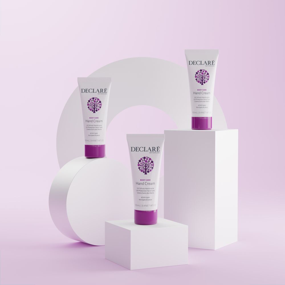 Drei Tuben Handcreme auf Podesten. Weiß, mit lila Verschluss. Aufschrift: DECLARE, Hand Cream, UV-Schutz, für alle Hauttypen.