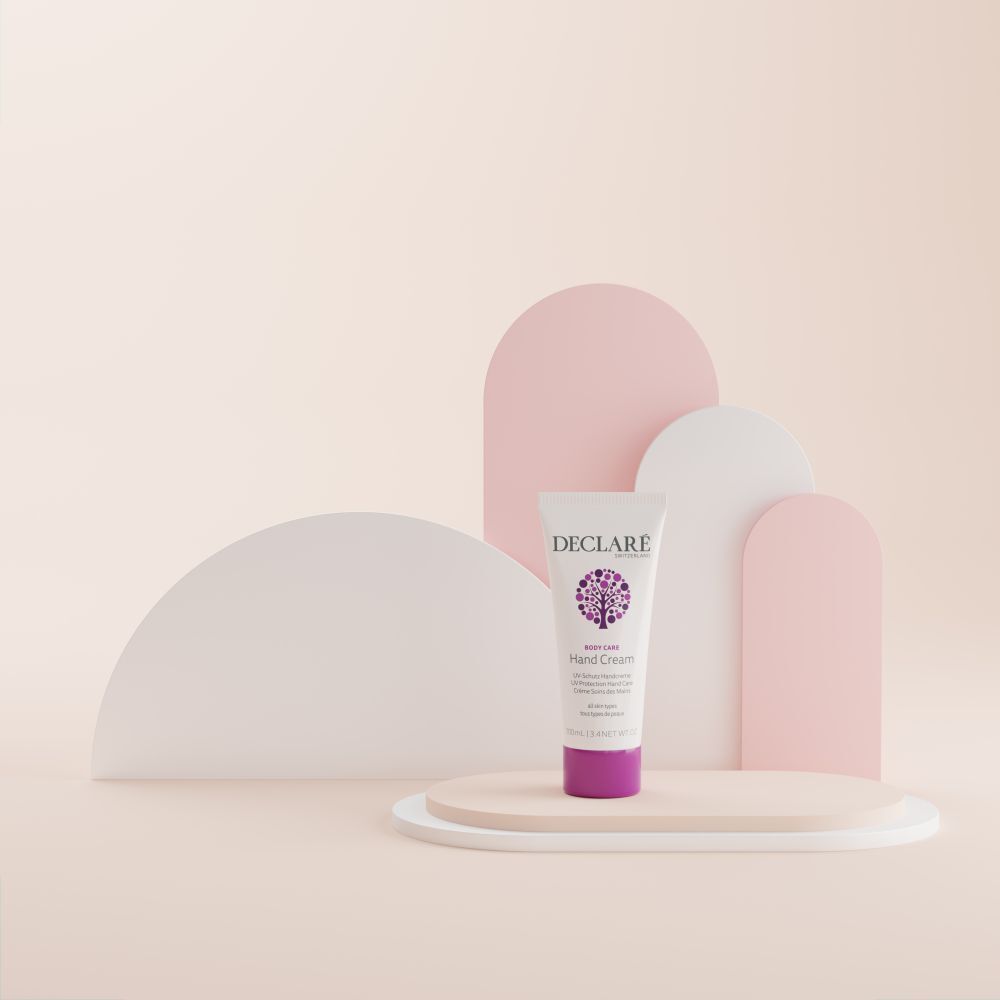 Eine Tube Handcreme auf einem Podest. Weiß, mit lila Verschluss. Aufschrift: DECLARE, Hand Cream, UV-Schutz, für alle Hauttypen.