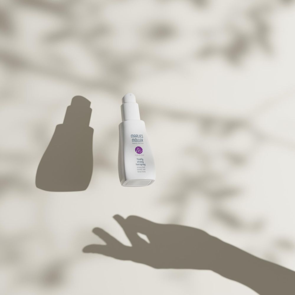 Eine weiße Pumpsprühflasche Marlies Möller Finally Strong Hairspray schwebt vor einem hellen Hintergrund mit Schatten.