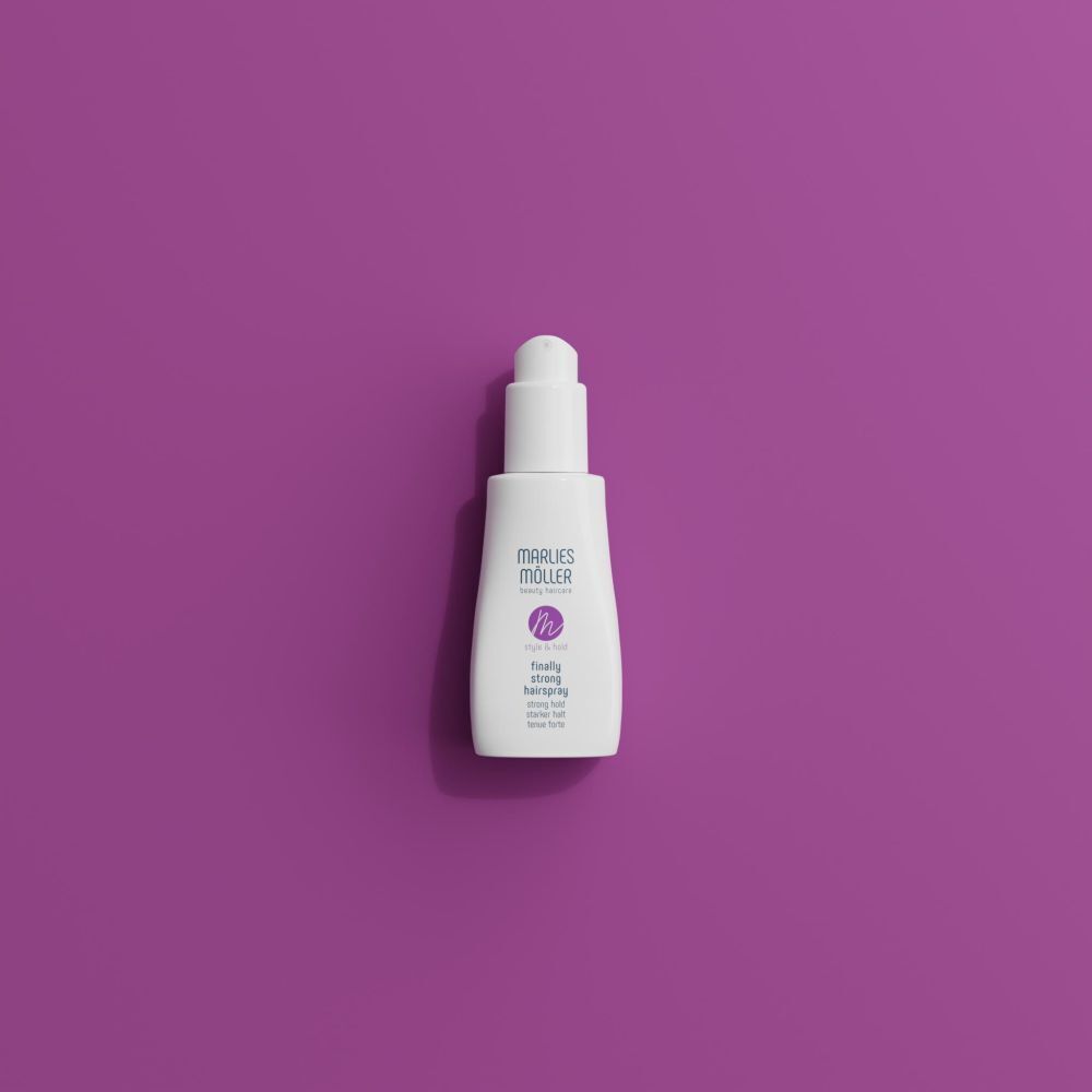 Eine weiße Pumpsprühflasche Marlies Möller Finally Strong Hairspray auf lila Hintergrund.