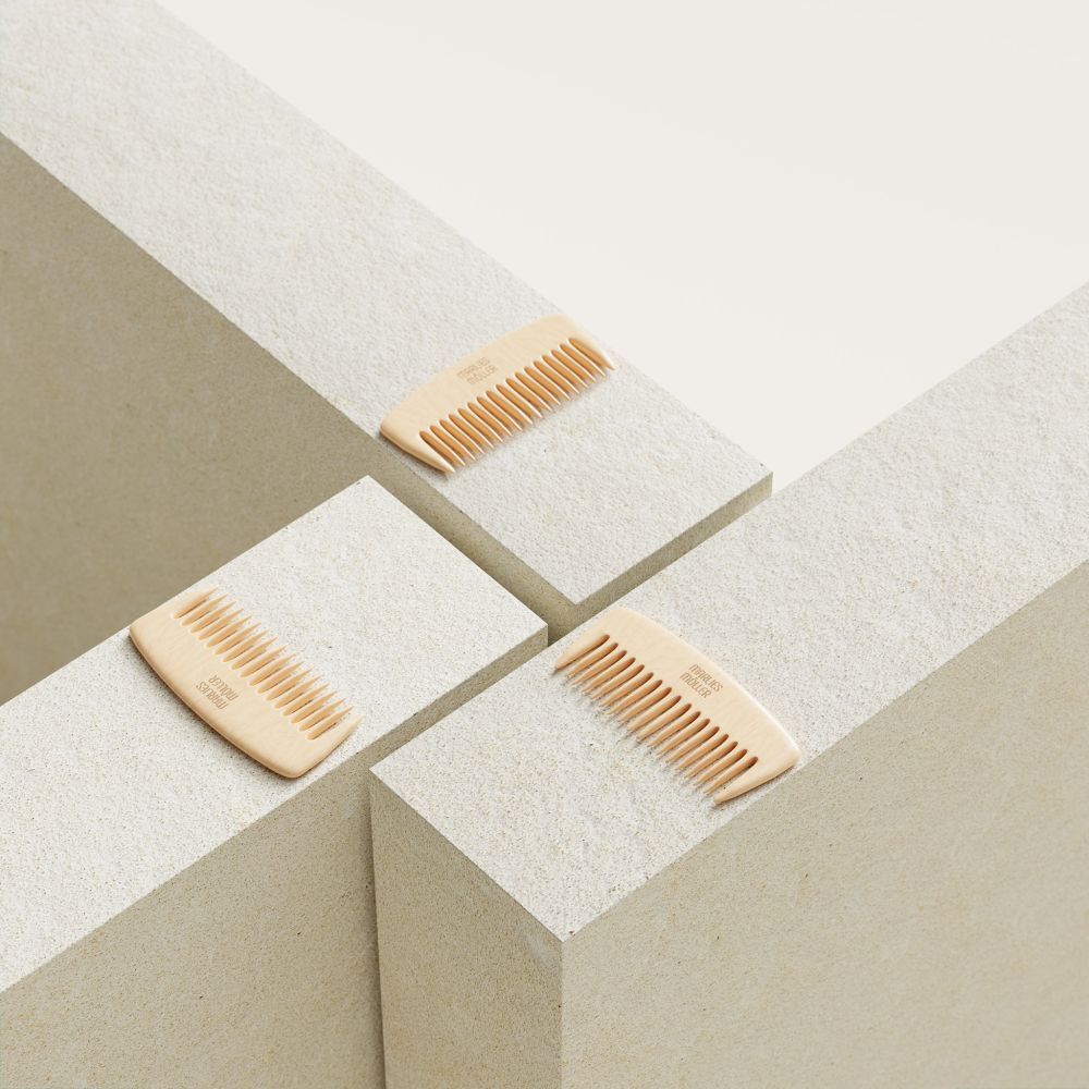 Trois peignes en bois sur des blocs blancs. Chaque peigne a une poignée arrondie et des dents fines. Le nom de la marque est visible.