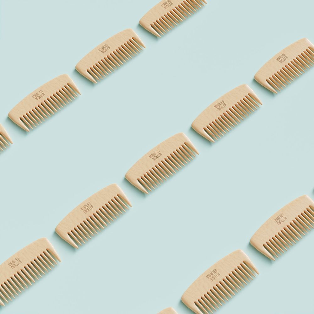 Plusieurs peignes en bois avec des poignées arrondies et des dents fines. Le nom de la marque est visible sur chaque peigne. Fond bleu clair.