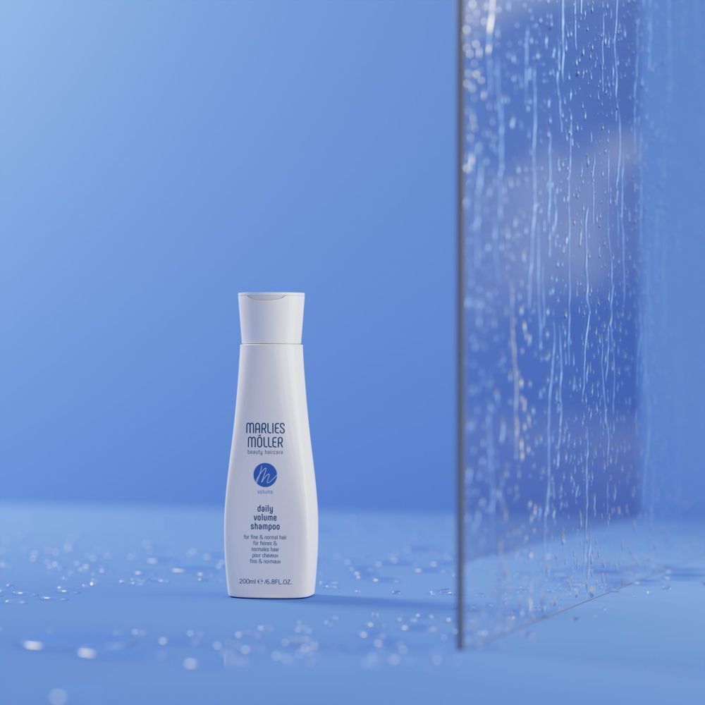 Eine weiße Flasche Marlies Möller Daily Volume Shampoo (200ml) vor blauem Hintergrund mit Wassertropfen.