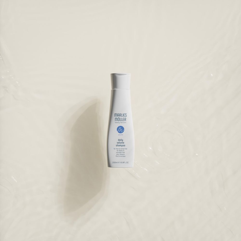 Un flacon blanc de Marlies Möller Daily Volume Shampoo sur fond clair avec des reflets d'eau.