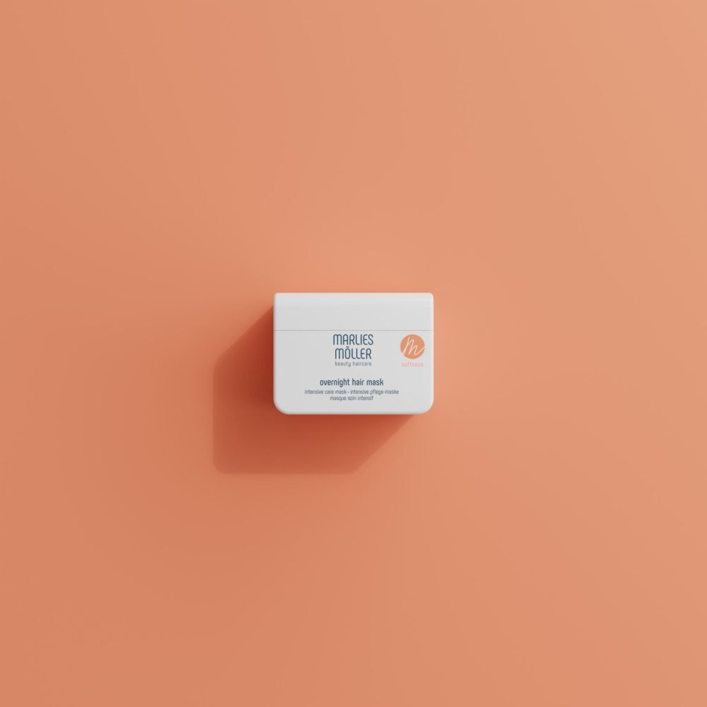 Weißer Tiegel mit Aufschrift MARLIES MÖLLER. Text: overnight hair mask. Orangefarbenes Logo. Der Tiegel liegt auf orangefarbenem Hintergrund.
