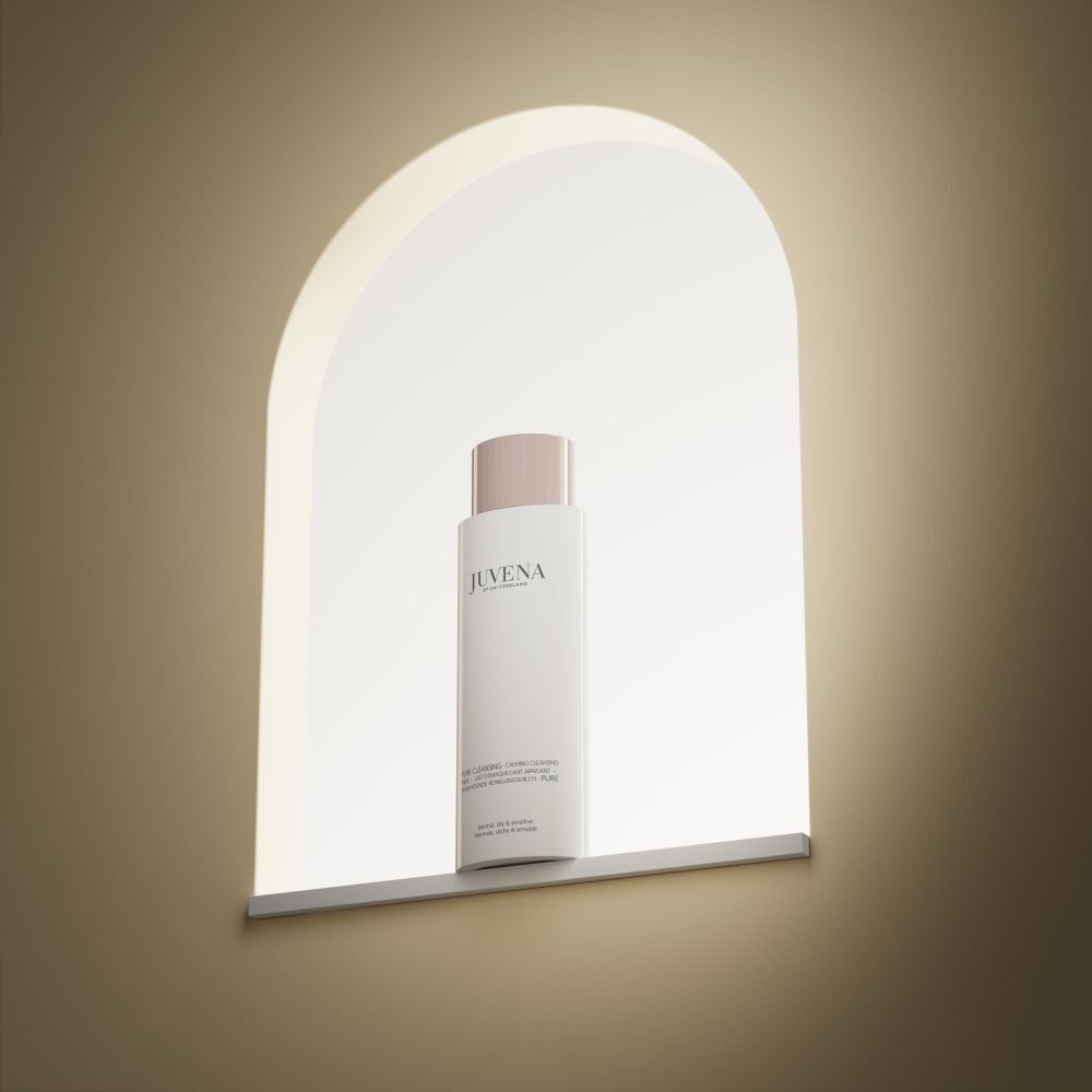 Un flacon blanc de Juvena Pure Cleansing Calming Cleansing Milk avec bouchon rose dans une niche éclairée.