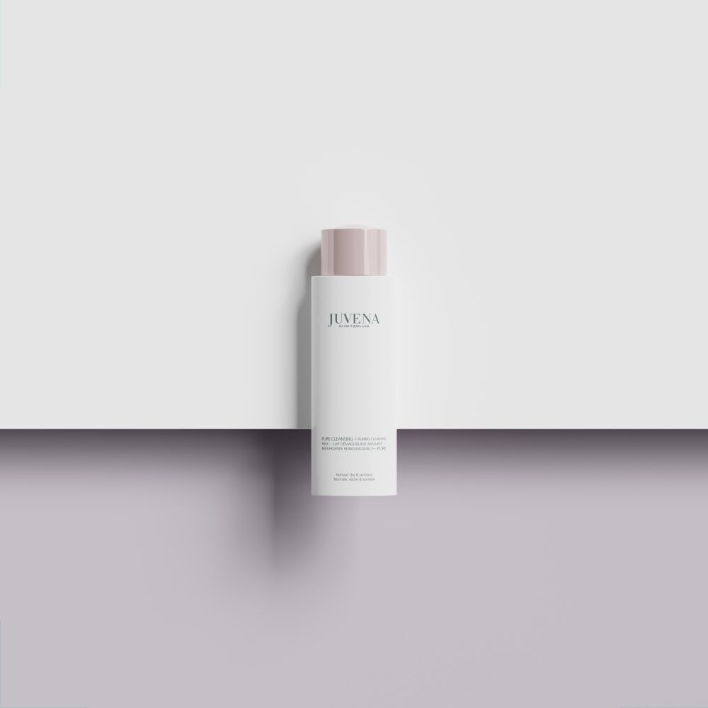 Un flacon blanc de Juvena Pure Cleansing Calming Cleansing Milk avec bouchon rose sur une surface blanche.