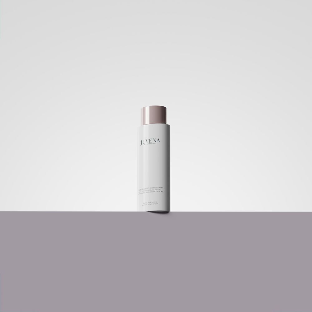 Un flacon blanc de Juvena Calming Cleansing Milk avec bouchon rose sur un socle gris.