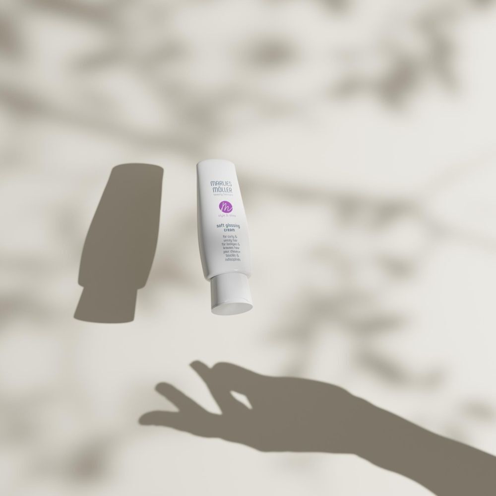 Un tube blanc avec logo et texte violets. Inscription: MÖLLER, Soft Glossing Cream. Ombres de main et feuilles.