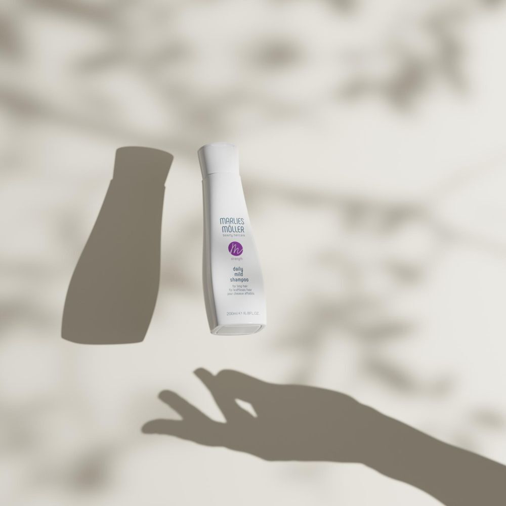 Un flacon blanc avec bouchon blanc et ombres d'une main et de feuilles. Le flacon porte "Marlies Möller" et "daily mild shampoo".