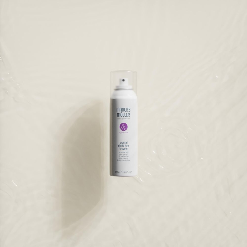 Flacon spray blanc avec bouchon transparent. Inscription: MARLIES MÖLLER, crystal shine hair lacquer, style & hold. Sur fond clair.
